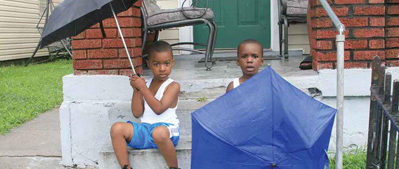 Two young boys with umbrellas sitting on steps in front of a house