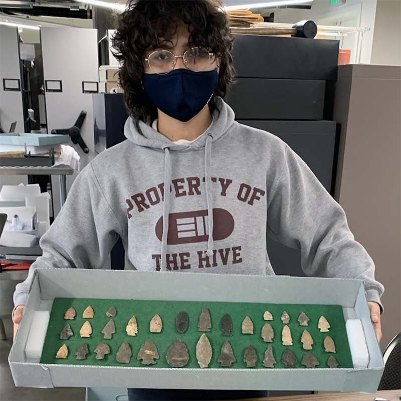 A photograph of a student holding up a box full of stone arrowheads