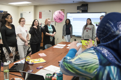 group of students doing interactive activity around a conference room table, person in hijab tossed pink ball to another classmate