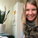 Lindsey Albracht, a white woman with blonde hair, sits at a desk smiling at the camera. A tortoiseshell cat sits in her lap. 