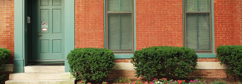 The front entrance of the Honors House, a brick building lined with bushes and flowers.