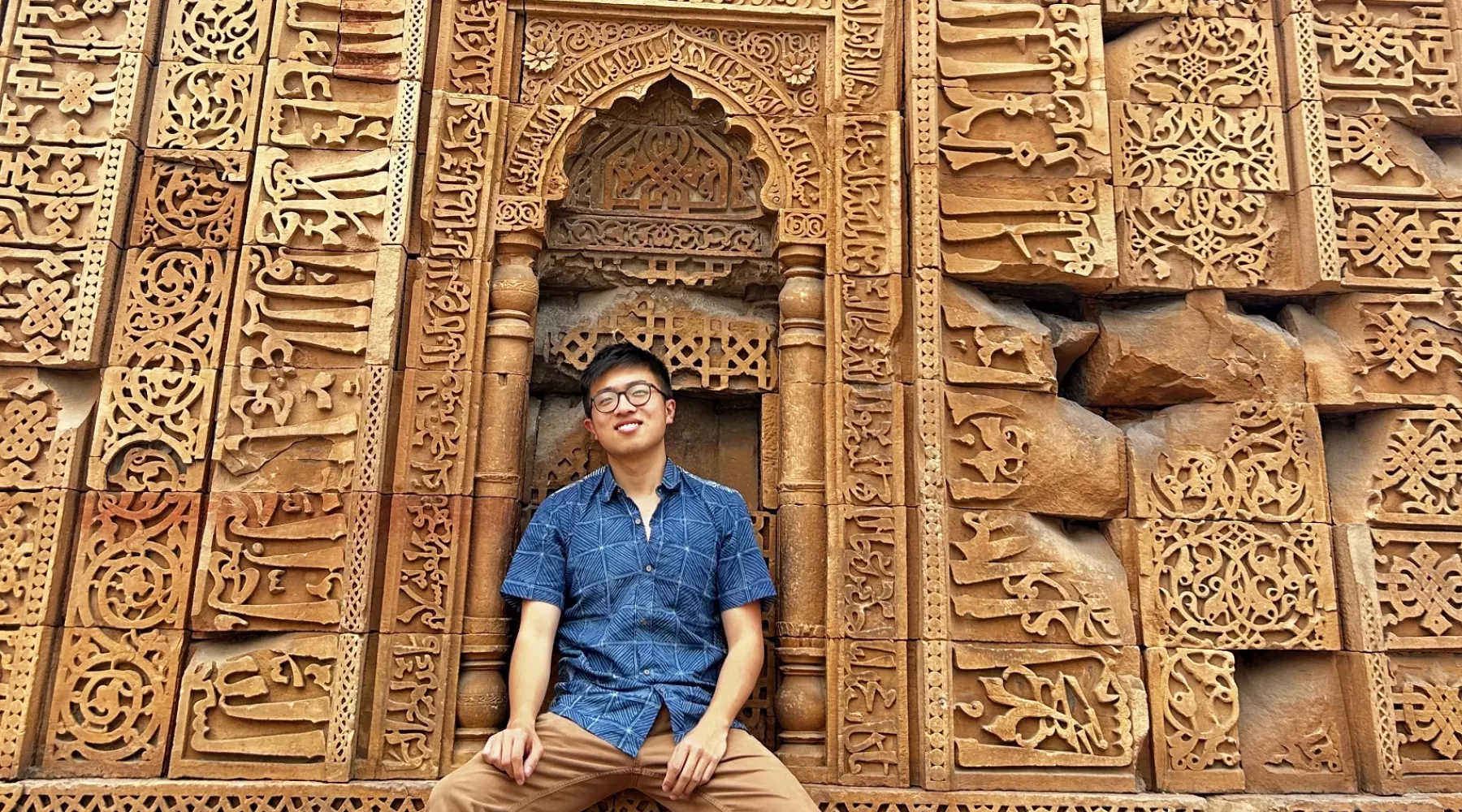 UofL student sits in front of a wall with intricate carvings and engravings in India.