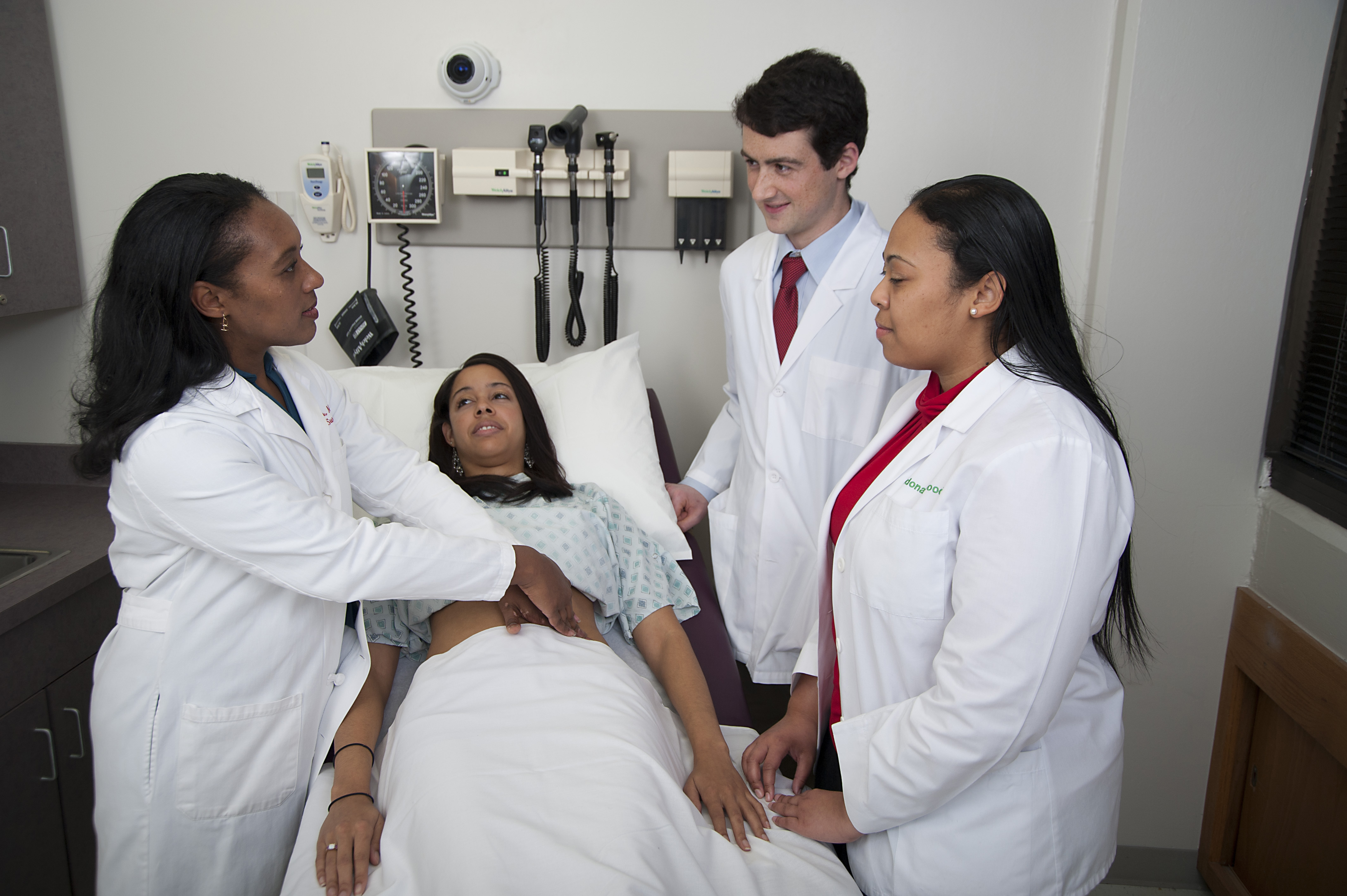 two students observe as a faculty person demonstrates the abdominal exam on a standardized patient
