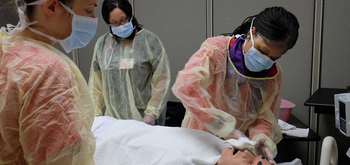 Photo of two nrusing students in a simulation lab with a mannequin overseen by faculty with overlay that reads 'We are ready for you.'