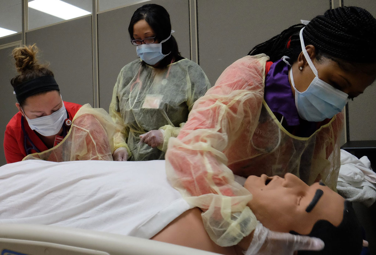 Photo of three nursing students providing care to a manikin patient during a nursing simulation.