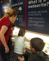 Kids and instructor looking at meteorite exhibit in planetarium lobby.