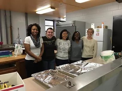 students smiling and preparing to serve food.