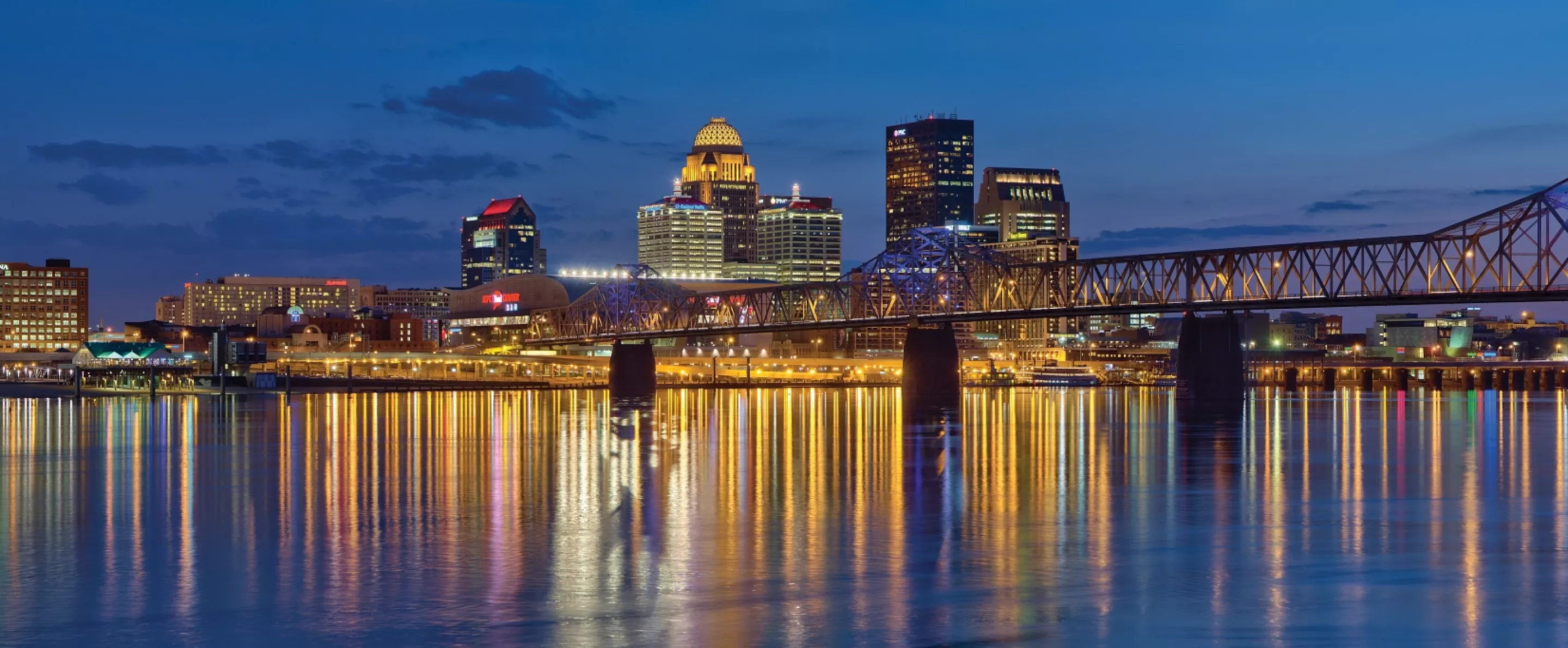 Nighttime skyline photo of the Louisville waterfront with light reflections in the Ohio River