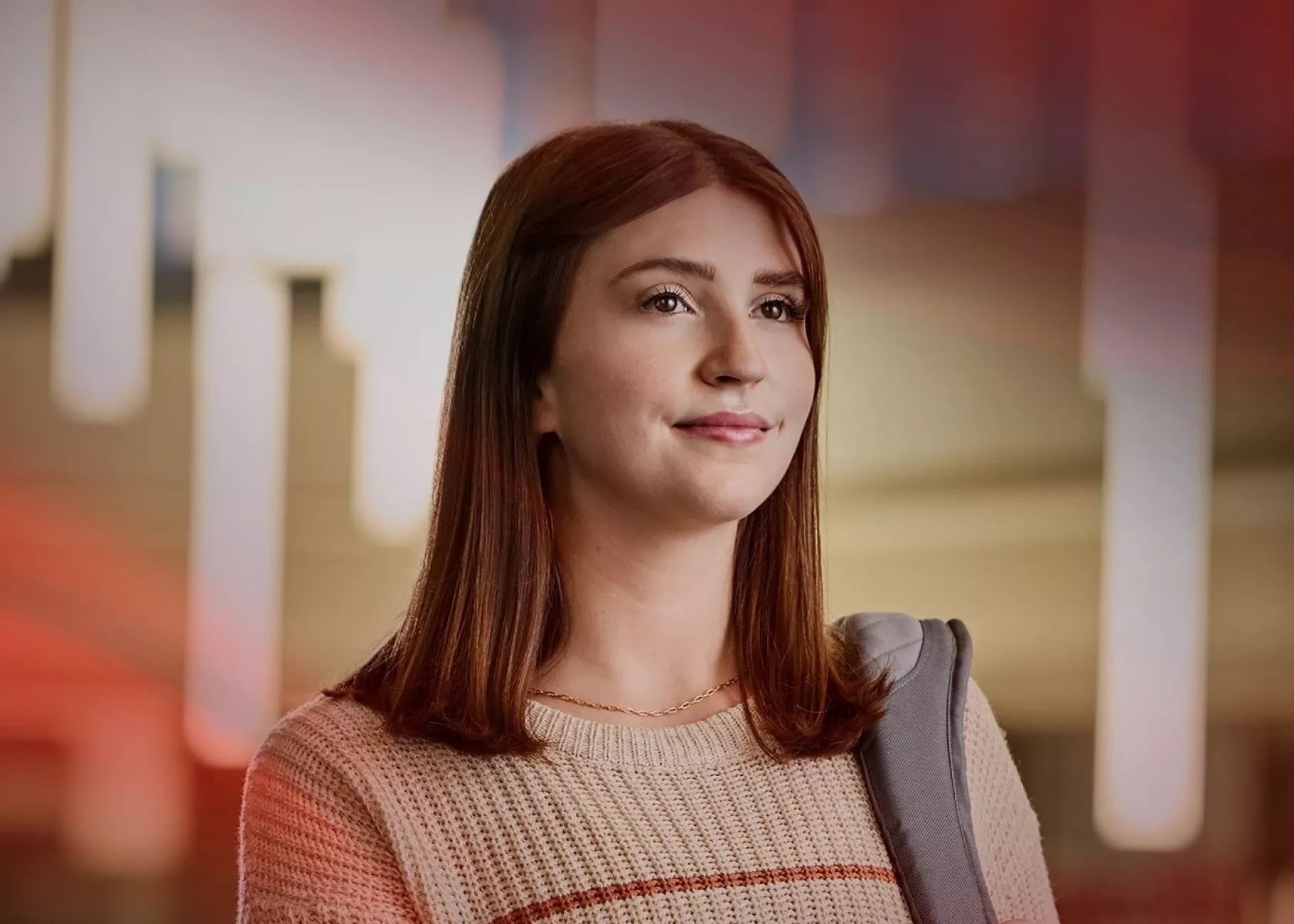 A student with a striped sweater and backpack stands on a glass balcony.