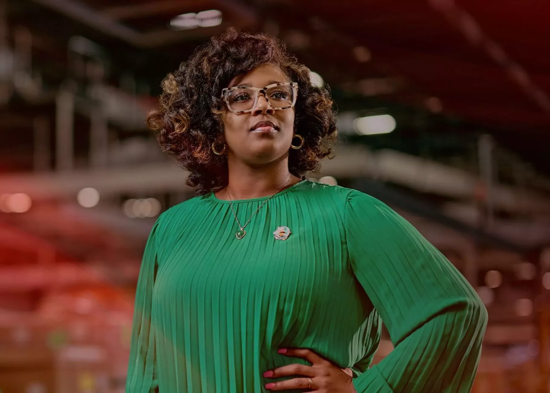 A woman in a green blouse poses confidently in a shipping warehouse.