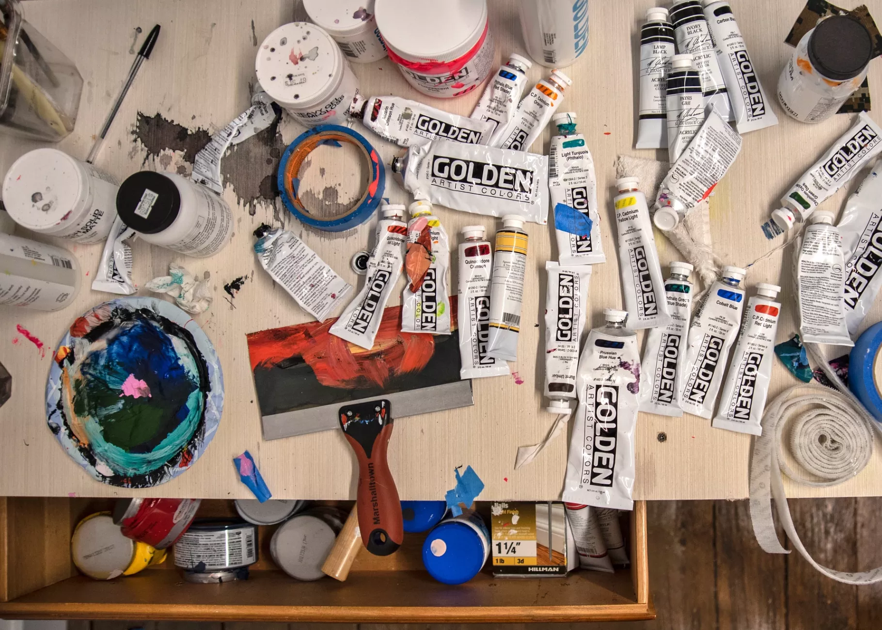 Artist's workspace including paints, trays, and tape