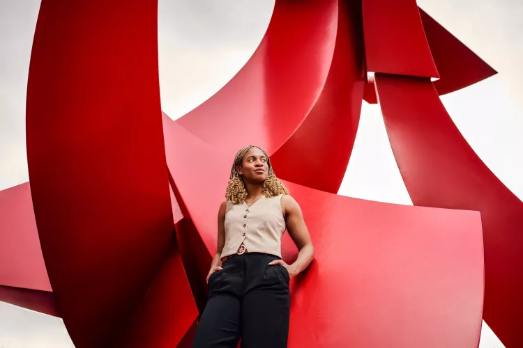 A confident young woman poses with hands in pocket against a large red sculpture.