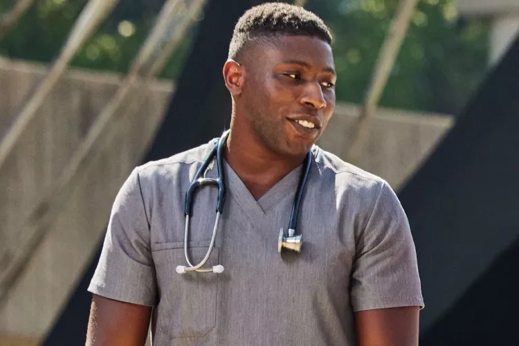 A man in gray medical scrubs with a stethoscope having a conversation outside.