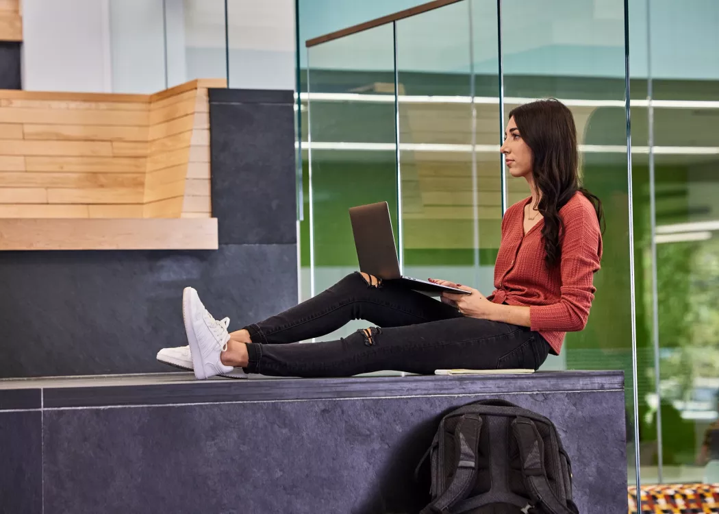 Student sitting on the front entrance steps to the Belknap Academic center in deep thought while typing on the computer.