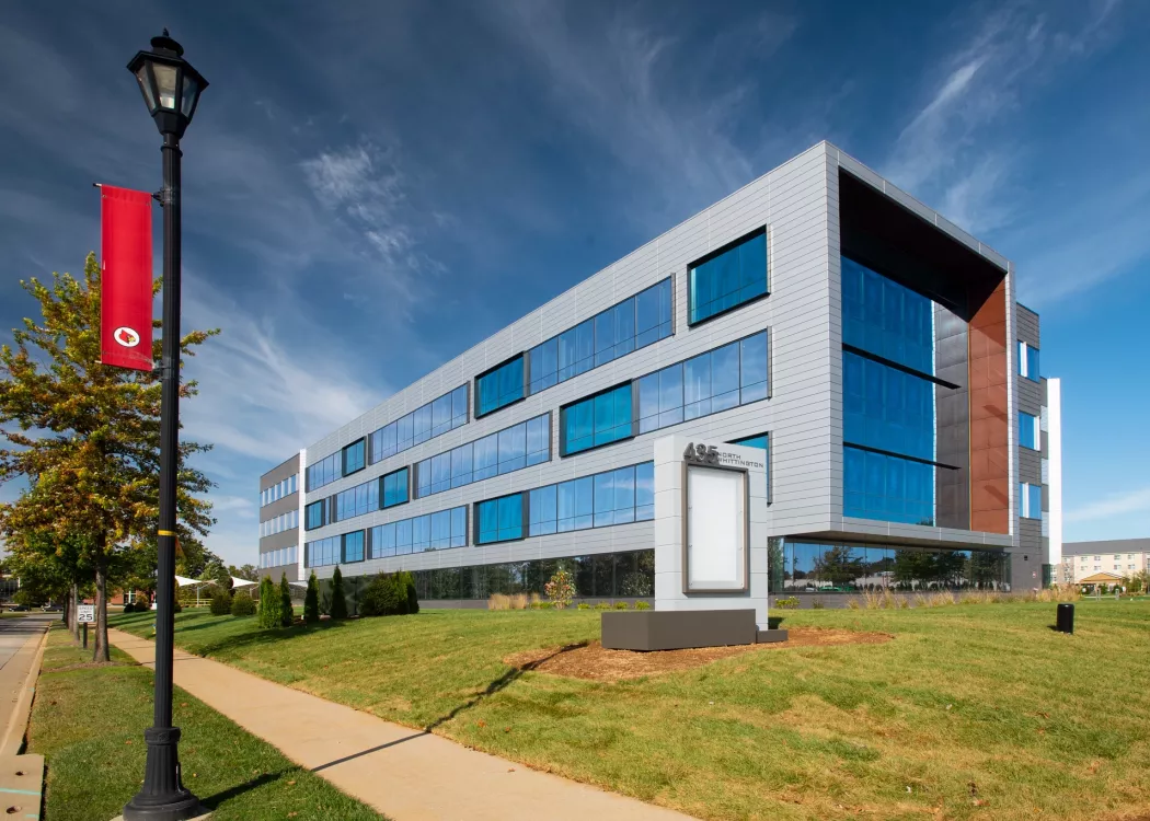 A long rectangular modern building newly produced for UofL. A lamp post with a UofL logo can be seen in front of the building.