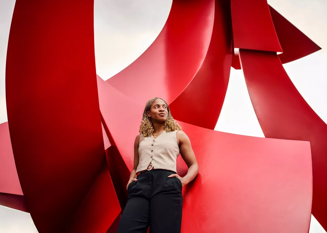 A confident young woman poses with hands in pocket against a large red sculpture.