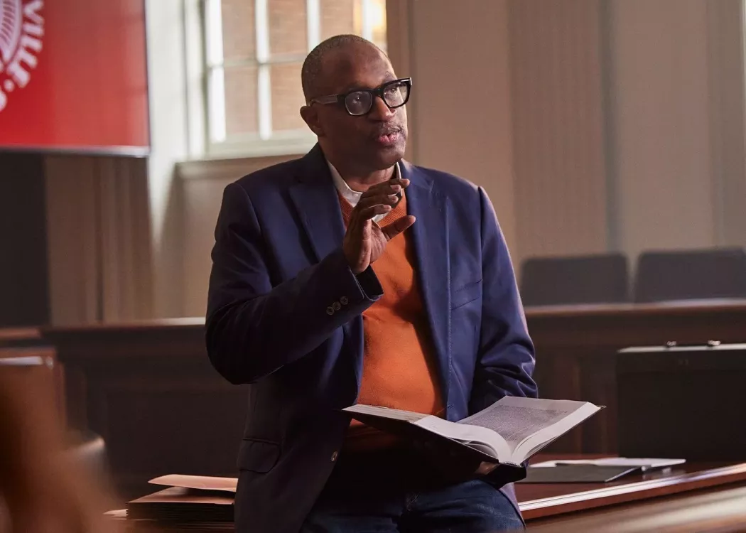 A professor with glasses and holding a book lectures in a school courtroom.