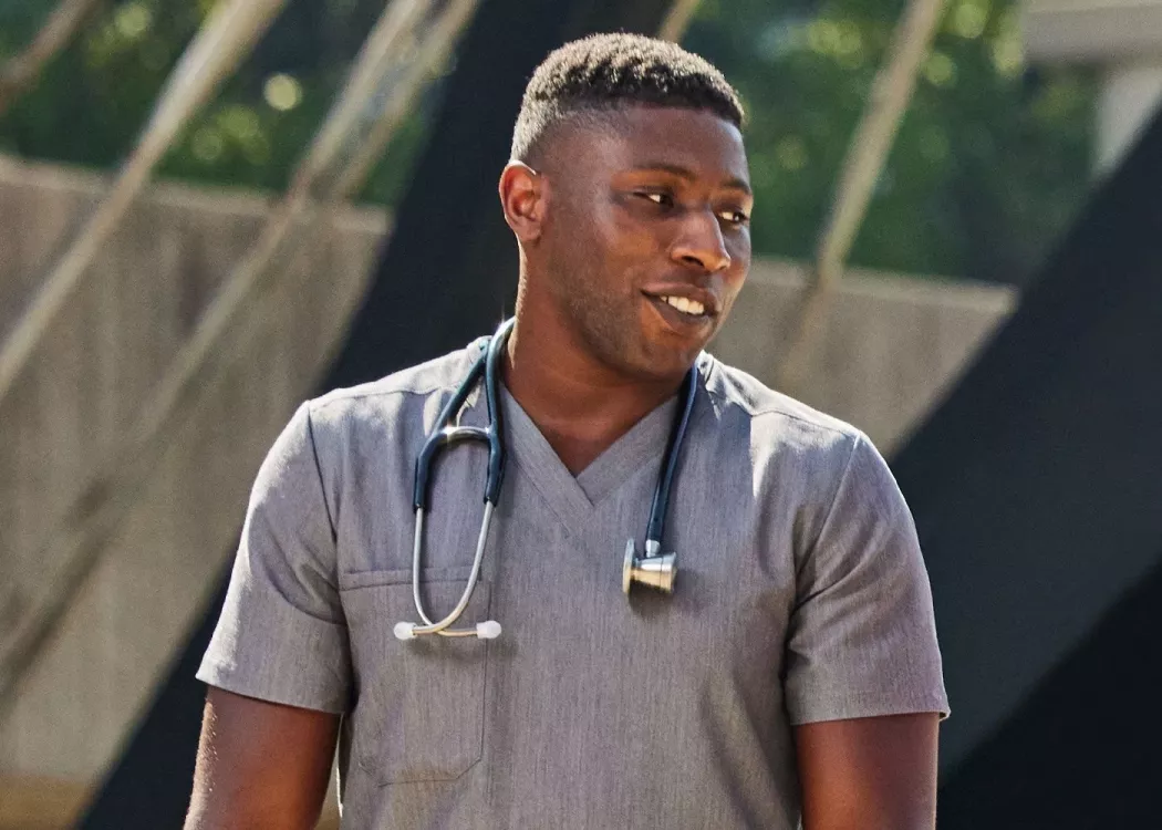 A man in gray medical scrubs with a stethoscope having a conversation outside.