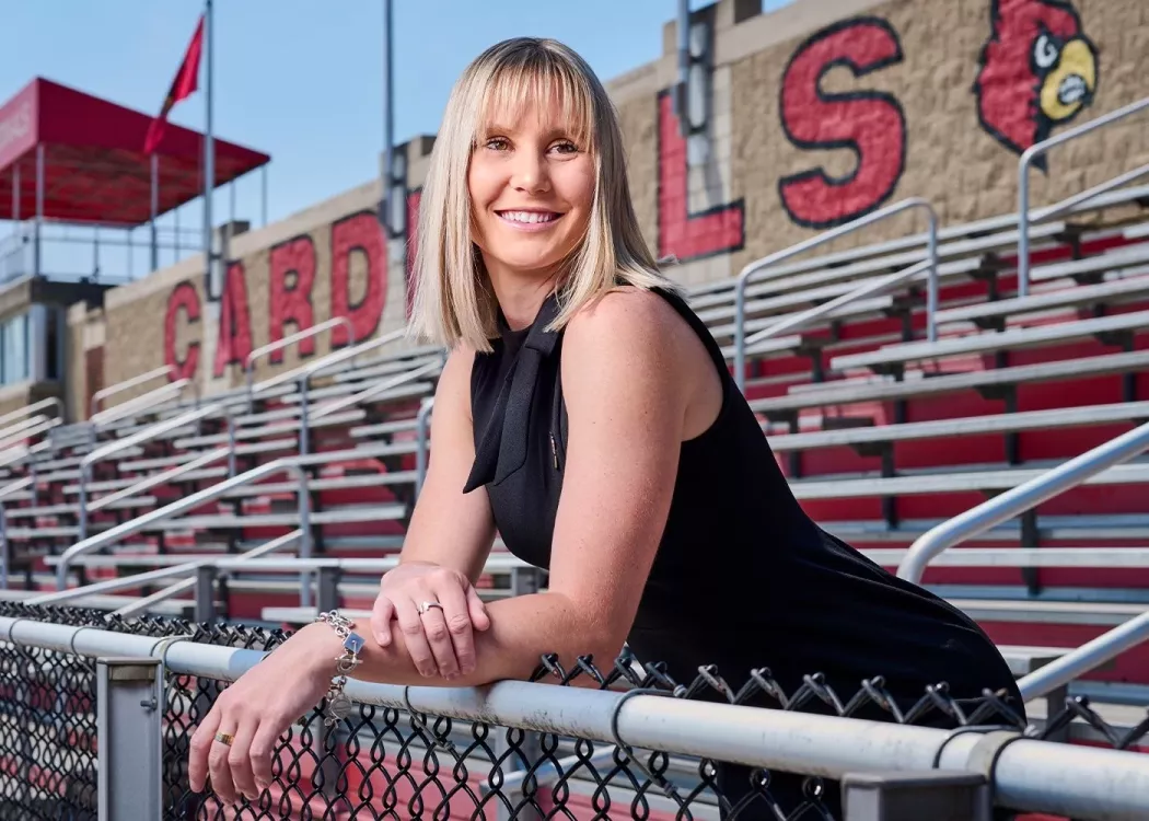 A smiling young woman standing among outdoor stadium bleachers.