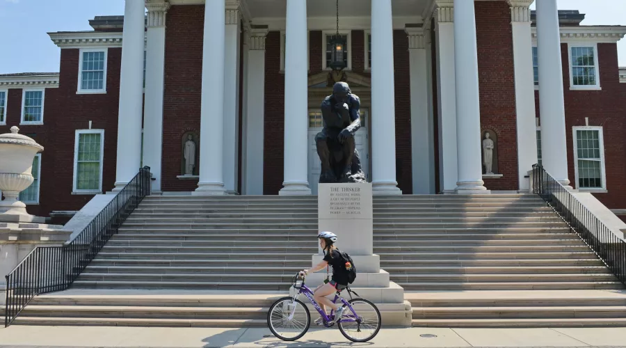 Student biking past the Thinker in front of Grawemeyer Hall