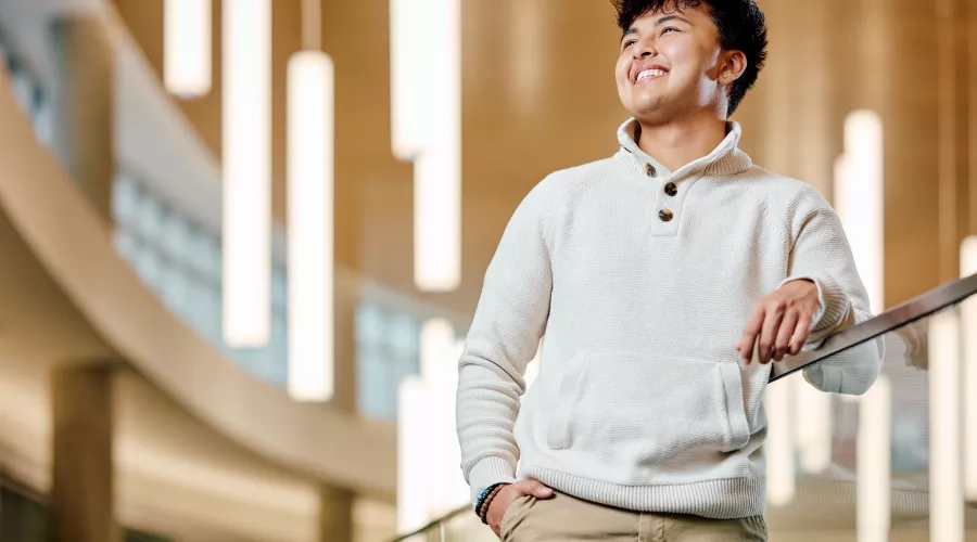 A smiling young male student standing on a modern indoor balcony