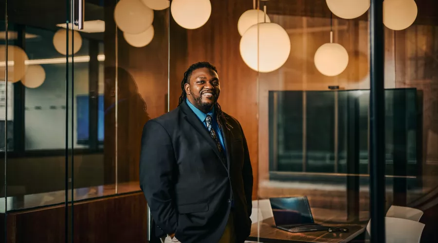 A smiling man in a suit standing in a modern office space.