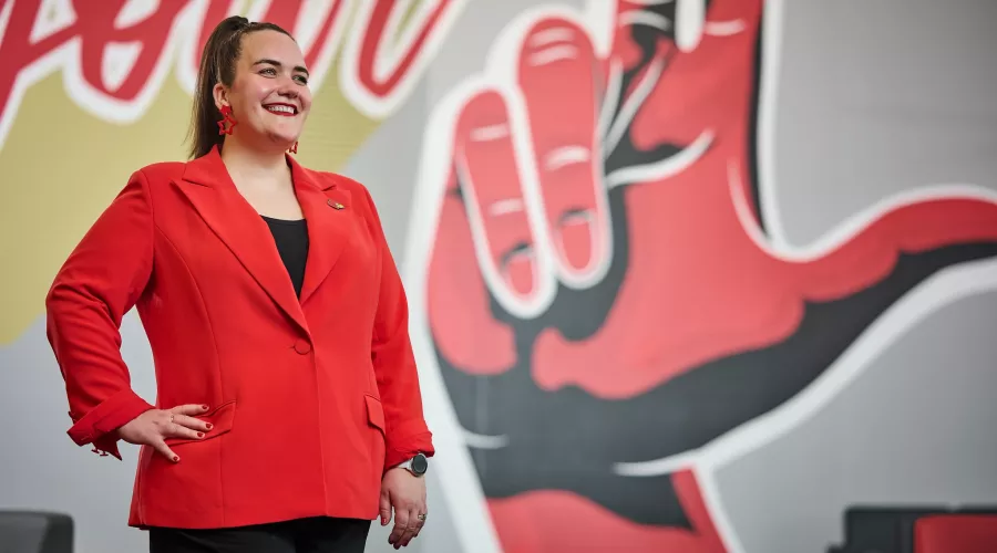 A smiling woman in a red blazer standing in front of an indoor mural.