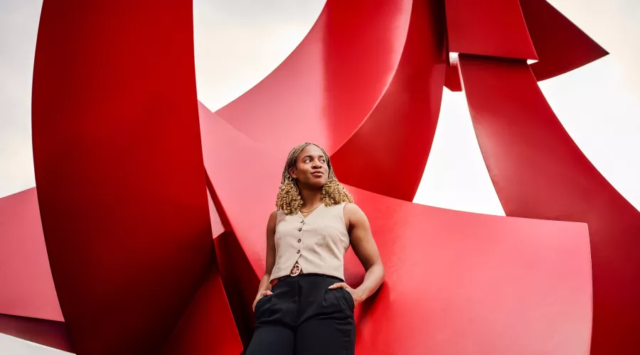 A confident young woman poses with hands in pocket against a large red sculpture.