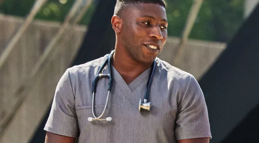 A man in gray medical scrubs with a stethoscope having a conversation outside.