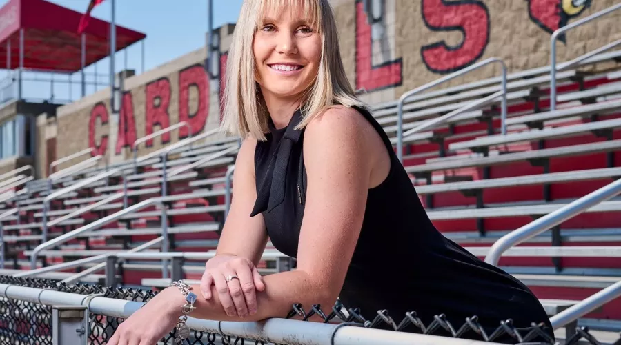 A smiling young woman standing among outdoor stadium bleachers.