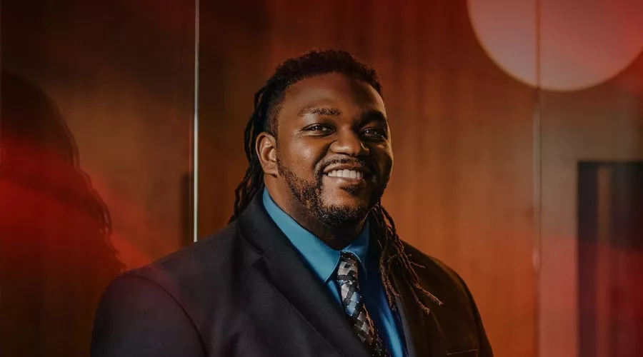 A smiling man in a dark suit posed in an office setting.