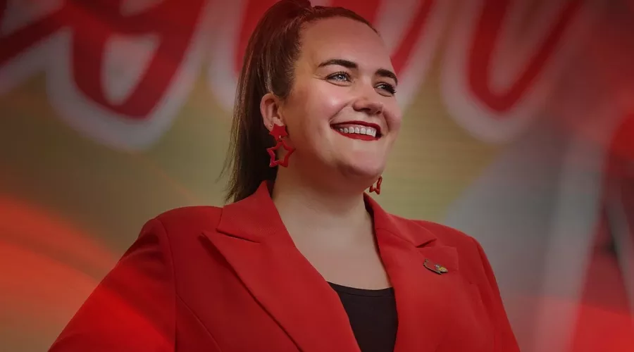 A smiling woman in a red blazer poses in front of an indoor mural.