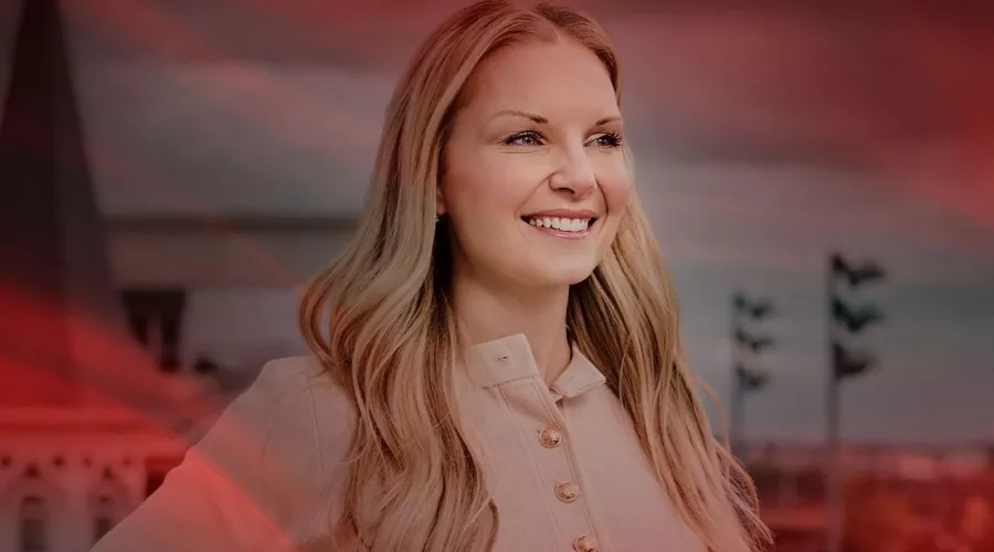A smiling woman stands on a balcony in front of Churchill Downs' twin spires.