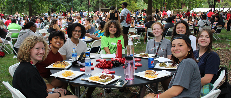 Smiling students sitting around an outdoor table with food.