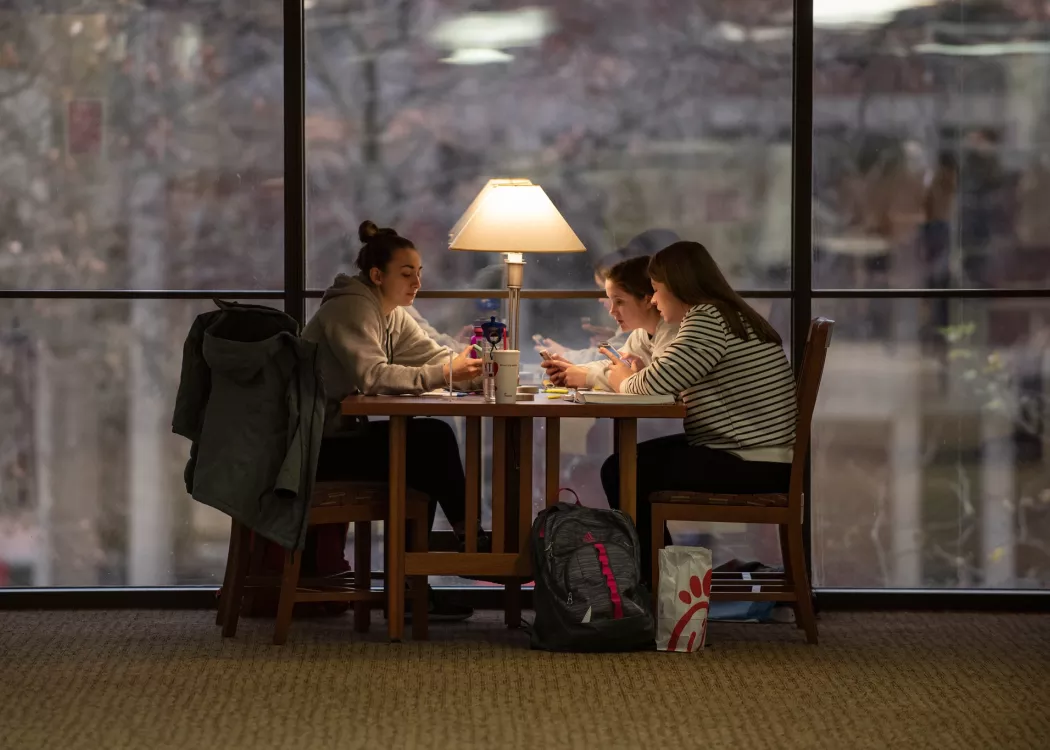 Three students study together at a table near the windows in Ekstrom Library